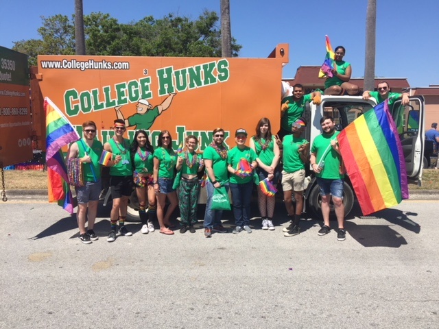 College Hunks Hauling Junk team members posing with rainbow flags and beads (and a moving truck).