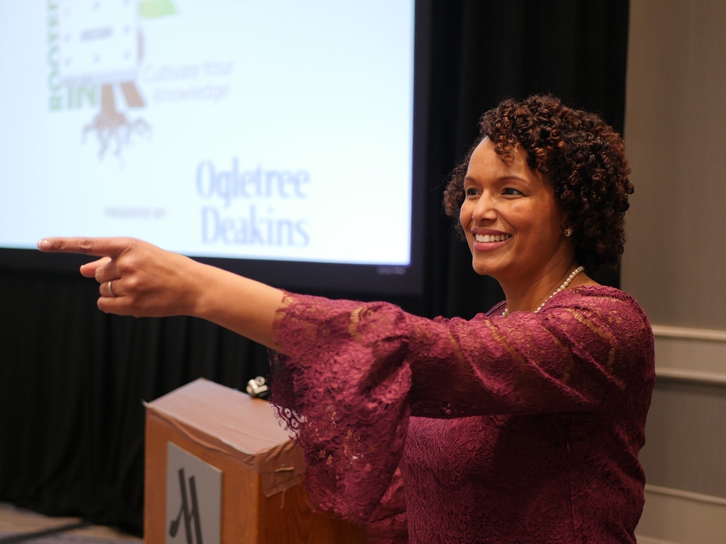 Heather Younger, speaking in a conference setting, gesturing to the attendees.