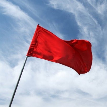 A red flag waves against a cloudy sky.