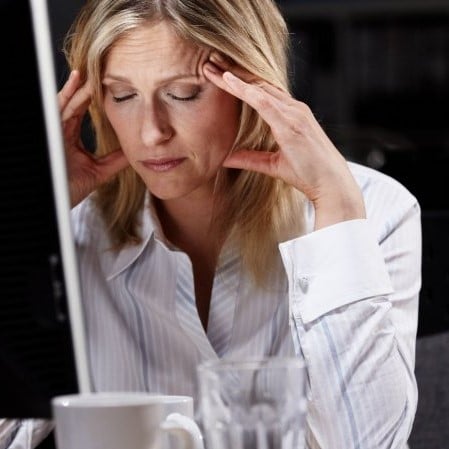 A woman rubs her temples while wearing a pained expression in front of a computer