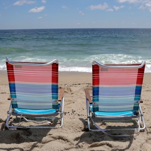 Two empty beach chairs face a tropical horizon.
