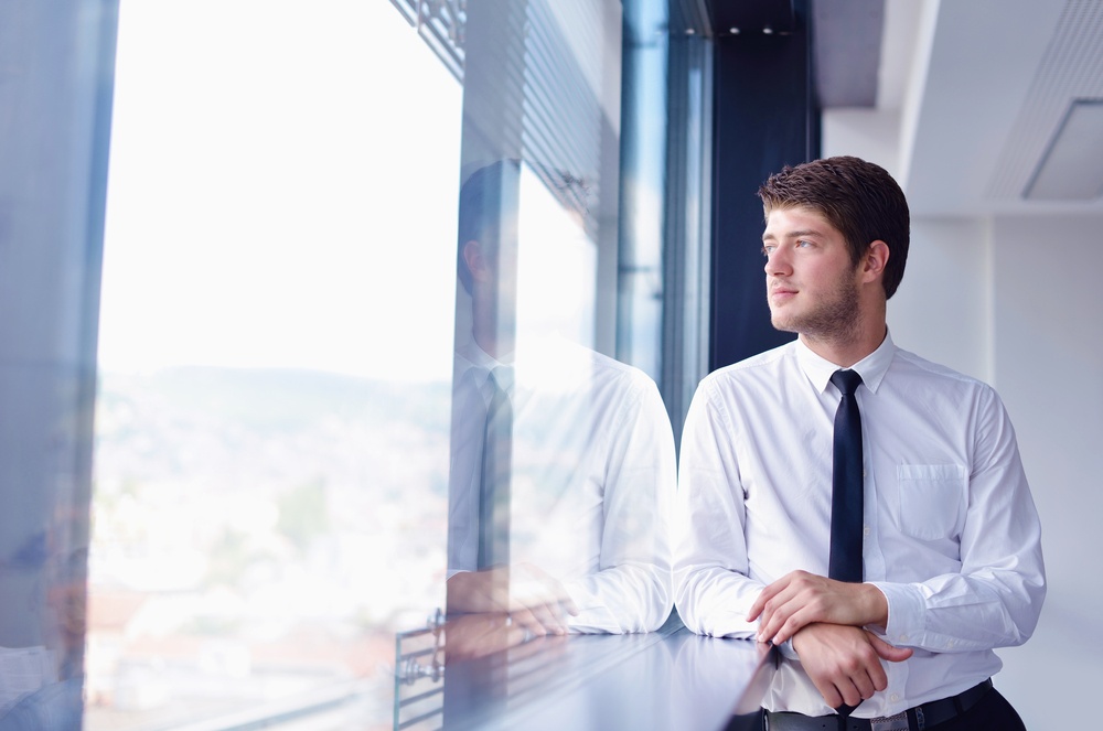 happy young business  man work in modern office looks at his reflection in the window